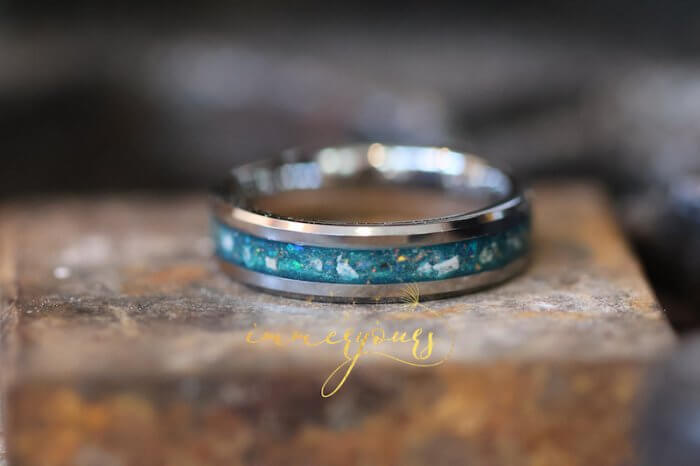 A close-up of a tungsten memorial ash ring with a vibrant blue inlay. The inlay includes a mixture of blue and iridescent flakes, creating a captivating and vibrant appearance.